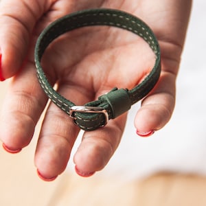 May include: A green leather bracelet with white stitching and a silver buckle.