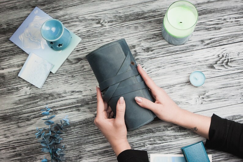 May include: A blue leather notebook with a strap closure, held by a person's hands on a wooden surface.