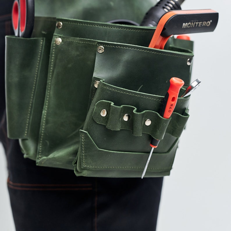 May include: A green leather tool belt with multiple pockets and a variety of tools, including a screwdriver, pliers, and a small tool with the word "MONTERO" on it.