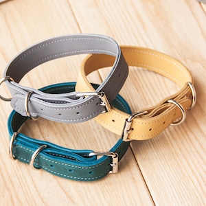 May include: Three leather dog collars in gray, yellow, and teal. The collars are stacked on top of each other, with the gray collar on top.