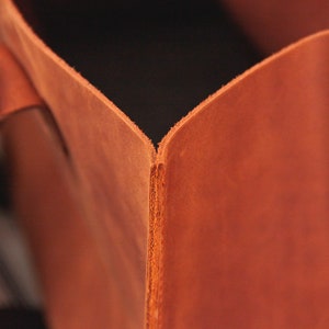 May include: Close-up of the inside corner of a brown leather tote bag. The leather is smooth and has a slight sheen.