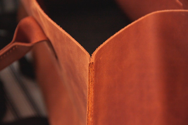 May include: Close-up of the inside corner of a brown leather tote bag. The leather is smooth and has a slight sheen.