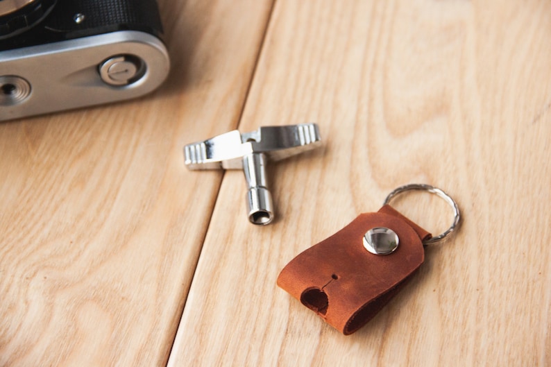 May include: A silver-toned camera lens wrench and a brown leather key chain with a silver ring and button.