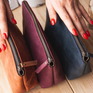 May include: Three leather zippered pouches in brown, burgundy, and navy blue.