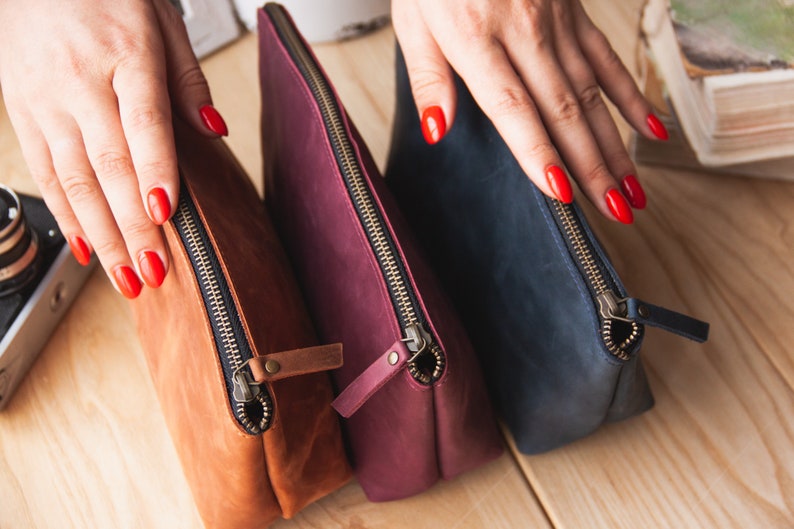 May include: Three leather zippered pouches in brown, burgundy, and navy blue.