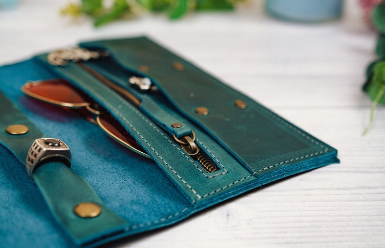 May include: A teal leather wallet with a zipper closure, a ring holder, and a glasses compartment. The wallet is open and the zipper is pulled down.