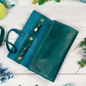 May include: Teal leather jewelry roll with a strap and multiple compartments for storing rings, earrings, and necklaces.