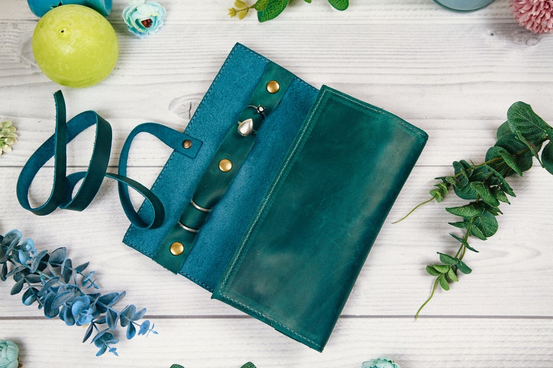 May include: Teal leather jewelry roll with a strap and multiple compartments for storing rings, earrings, and necklaces.