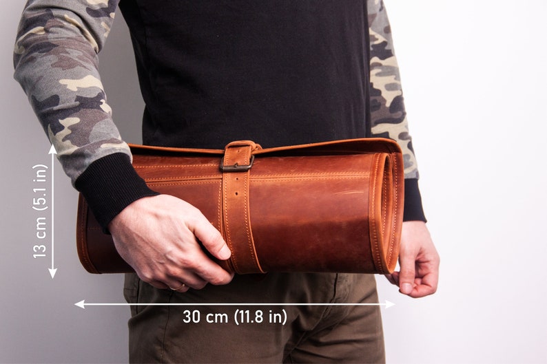 Peut inclure: Un sac enroulable en cuir marron avec une fermeture &agrave; boucle. Le sac mesure 30 cm de large et 13 cm de haut.