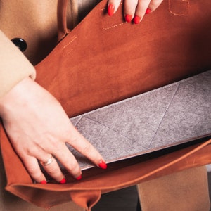 May include: A brown leather tote bag with a gray felt insert. The bag is open and the felt insert is visible.