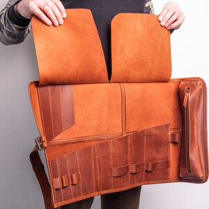 Peut inclure: Un &eacute;tui enroulable en cuir marron avec plusieurs compartiments et une poche zipp&eacute;e. L'&eacute;tui est ouvert pour r&eacute;v&eacute;ler l'int&eacute;rieur, qui comporte plusieurs fentes pour ranger des outils ou d'autres objets.