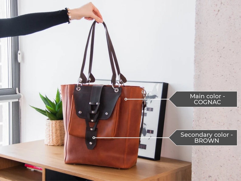 K&ouml;nnte beinhalten: Eine braune Ledertasche mit einer schwarzen Lederklappe und einem Rei&szlig;verschluss. Die Tasche hat einen oberen Griff und einen Schultergurt.