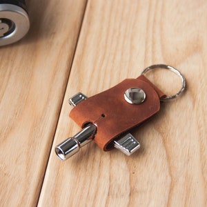 May include: A brown leather keychain with a silver multi-tool attached. The keychain has a silver ring for attaching keys.