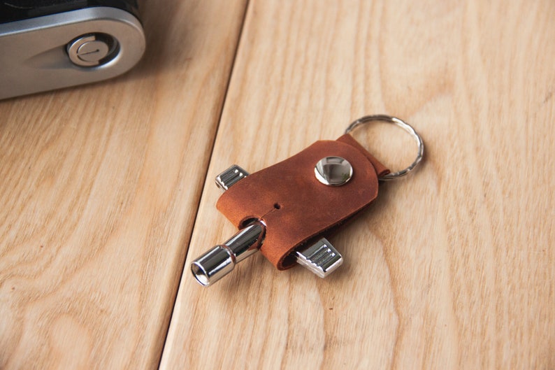 May include: A brown leather keychain with a silver multi-tool attached. The keychain has a silver ring for attaching keys.