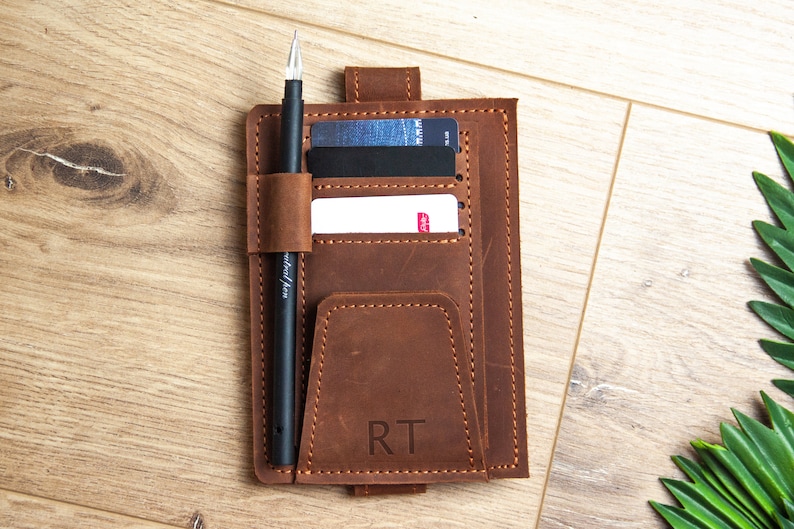 May include: A brown leather notebook cover with a pen holder, card slots, and a pocket. The cover has the initials "RT" embossed on the front.