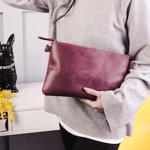 Peut inclure: Une pochette en cuir bordeaux avec une fermeture &eacute;clair et une bandouli&egrave;re en cha&icirc;ne argent&eacute;e.