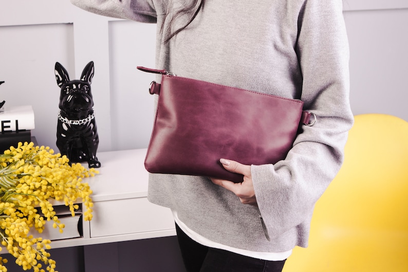 Peut inclure: Une pochette en cuir bordeaux avec une fermeture &eacute;clair et une bandouli&egrave;re en cha&icirc;ne argent&eacute;e.