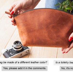 May include: A brown leather toiletry bag with a zipper closure. The bag is being held open by a hand with red nail polish.