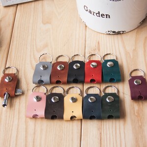 May include: A set of 12 leather keychains in various colors, including gray, brown, black, red, green, pink, yellow, blue, and burgundy. Each keychain has a silver ring and a silver button.
