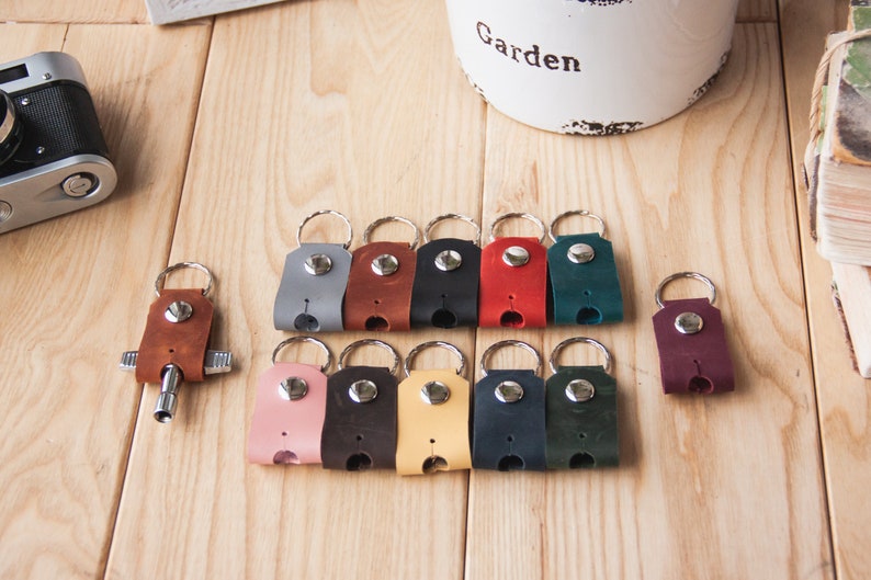 May include: A set of 12 leather keychains in various colors, including gray, brown, black, red, green, pink, yellow, blue, and burgundy. Each keychain has a silver ring and a silver button.