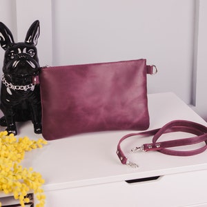 Peut inclure: Un sac &agrave; main en cuir bordeaux avec une bandouli&egrave;re en cha&icirc;ne argent&eacute;e. Le sac est pos&eacute; sur une surface blanche avec une figurine noire de bouledogue fran&ccedil;ais et un bouquet de mimosa jaune.