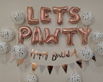 Könnte beinhalten: Ein Party-Dekorationssatz mit roségoldenen Folienbuchstaben, die "Let's Pawty" buchstabieren, und einem Banner mit der Aufschrift "Happy Birthday". Die Buchstaben und das Banner sind von weißen Ballons mit Pfotenabdrücken umgeben.