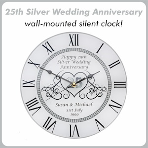 May include: White wall clock with black Roman numeral hour markers and black hands. The clock face has a silver heart design with the text "Happy 25th Silver Wedding Anniversary" and "Susan & Michael 31st July 1999".