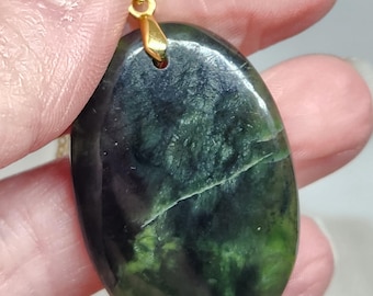 May include: A green and black oval pendant with a gold bail. The pendant is made of a natural stone with a unique pattern.