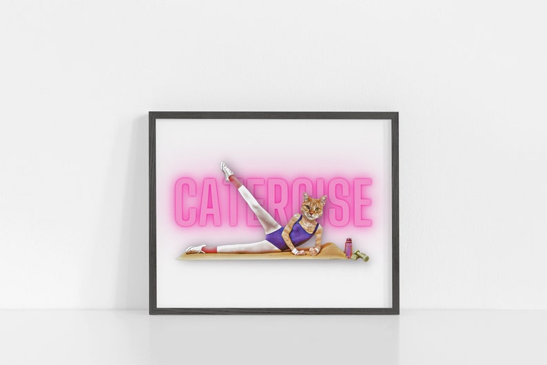 May include: A framed print of a cat wearing a leotard and leg warmers, doing a leg stretch on a yoga mat. The word "CATERCISE" is written in pink neon letters behind the cat.