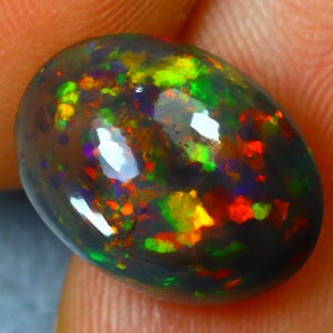 K&ouml;nnte beinhalten: Ein ovaler Opal-Edelstein in Dunkelgrau mit hohem Glanz. Der Opal zeigt eine Vielzahl von Farben, darunter Gr&uuml;n, Rot, Orange und Gelb.