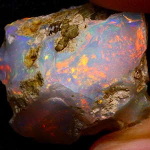 Könnte beinhalten: Ein roher, natürlicher Opal mit einer milchig weißen Basis und schillernden orangefarbenen, roten und blauen Blitzen.