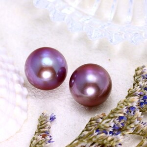 May include: Two iridescent purple pearls on a white background. The pearls are round and smooth, with a slight sheen.