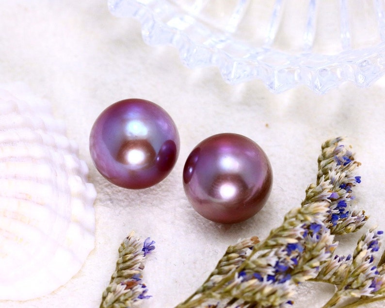 May include: Two iridescent purple pearls on a white background. The pearls are round and smooth, with a slight sheen.