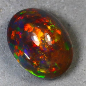 K&ouml;nnte beinhalten: Ein lebendiger, mehrfarbiger Opal-Edelstein mit einer dunklen Basis und Blitzen von Rot, Orange, Gr&uuml;n und Blau.