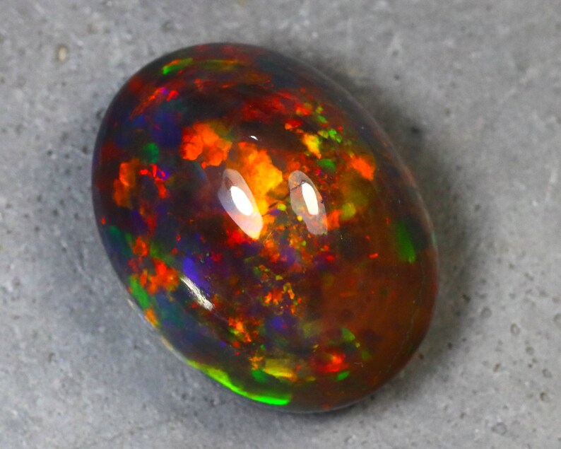 K&ouml;nnte beinhalten: Ein lebendiger, mehrfarbiger Opal-Edelstein mit einer dunklen Basis und Blitzen von Rot, Orange, Gr&uuml;n und Blau.
