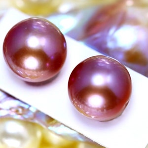 K&ouml;nnte beinhalten: Zwei irisierende rosa Perlen auf wei&szlig;em Hintergrund. Die Perlen sind rund und glatt, mit einem leichten Schimmer.