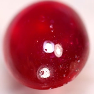 Könnte beinhalten: Nahaufnahme einer roten Glaskugel mit eingeschlossenen Luftblasen.
