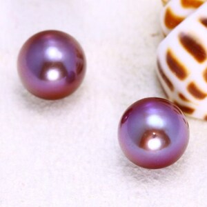 May include: Two iridescent purple pearls, one on the left and one on the right, on a white surface.