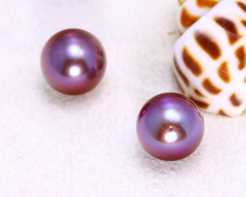 May include: Two iridescent purple pearls, one on the left and one on the right, on a white surface.