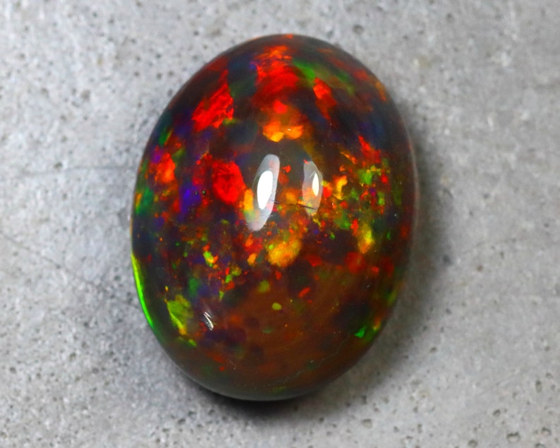 K&ouml;nnte beinhalten: Ein ovaler Opal-Edelstein in Dunkelbraun mit Schimmern in Rot, Gr&uuml;n und Blau.