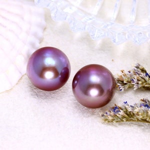 May include: Two iridescent purple pearls on a white surface with dried lavender flowers.