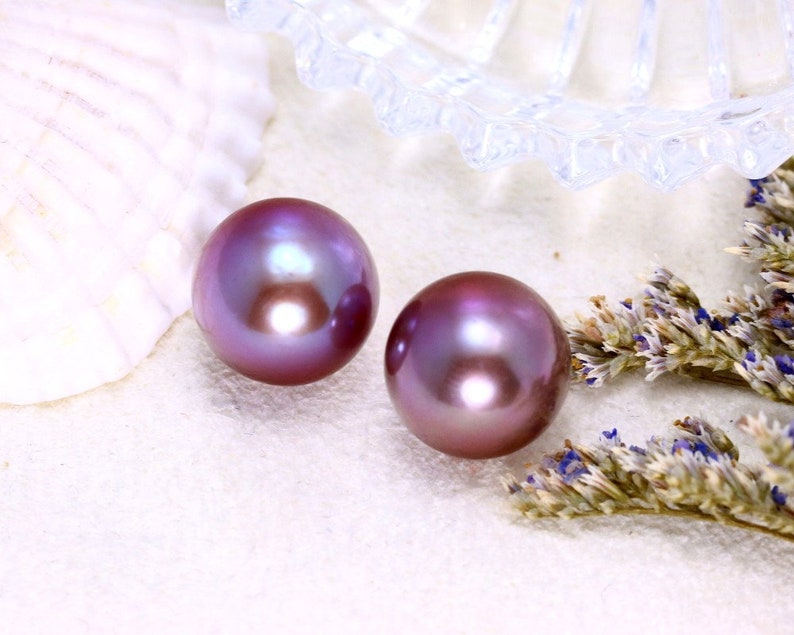 May include: Two iridescent purple pearls on a white surface with dried lavender flowers.