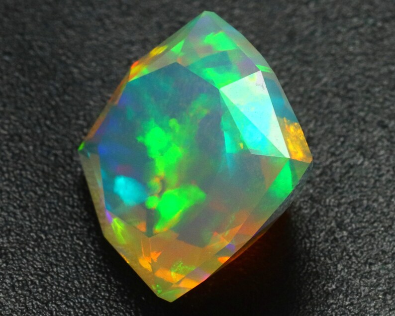 Op de afbeelding: Een gefacetteerde, iriserende opaal edelsteen met een kleurenspel in groen, blauw en oranje. De opaal is geslepen in een unieke, geometrische vorm.