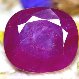 May include: A vibrant, deep pink oval-shaped gemstone with a faceted cut. The gemstone has a smooth, polished surface and is set against a white background.