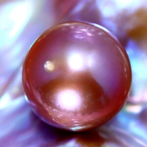 K&ouml;nnte beinhalten: Eine gro&szlig;e, irisierende, rosafarbene Perle mit einer glatten, runden Oberfl&auml;che.