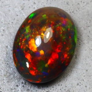 K&ouml;nnte beinhalten: Ein ovaler Opal-Edelstein in Dunkelgrau mit schwarzem Hintergrund. Der Opal hat eine Vielzahl von Farben, darunter Rot, Orange, Gelb, Gr&uuml;n und Blau.