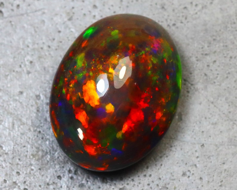 K&ouml;nnte beinhalten: Ein ovaler Opal-Edelstein in Dunkelgrau mit schwarzem Hintergrund. Der Opal hat eine Vielzahl von Farben, darunter Rot, Orange, Gelb, Gr&uuml;n und Blau.