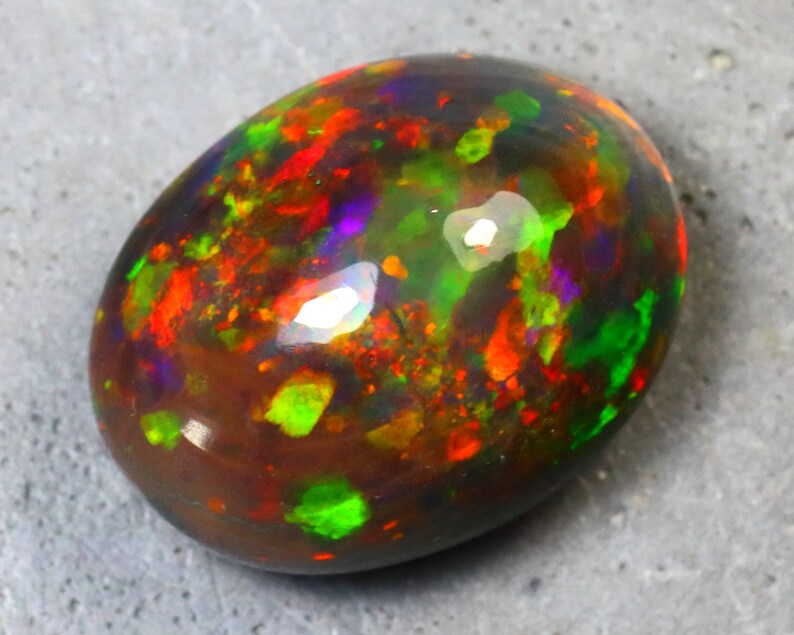 K&ouml;nnte beinhalten: Ein ovaler Opal-Edelstein in dunkelbraun mit Schimmern in Gr&uuml;n, Rot, Orange und Lila.