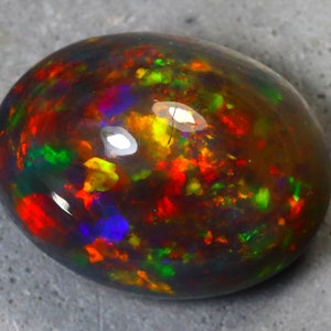 K&ouml;nnte beinhalten: Ein ovaler Opal-Edelstein in Dunkelgrau mit einem lebendigen Schimmer in Rot, Orange, Gelb, Gr&uuml;n, Blau und Violett.