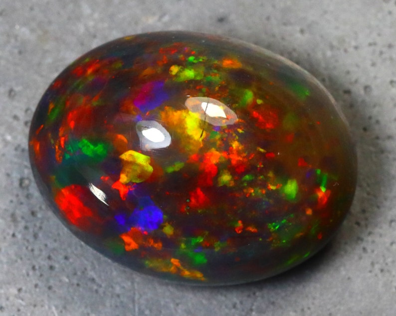 K&ouml;nnte beinhalten: Ein ovaler Opal-Edelstein in Dunkelgrau mit einem lebendigen Schimmer in Rot, Orange, Gelb, Gr&uuml;n, Blau und Violett.
